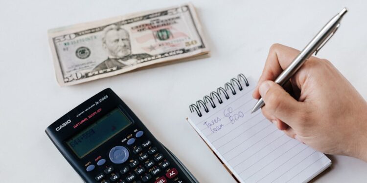 a hand holding a pen and a notebook next to a calculator