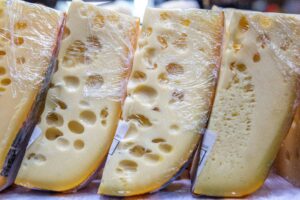 Rustic wheel of grouse cheese on wooden board with herbs and bread.